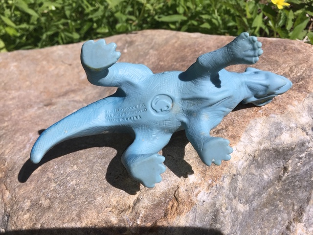 Underside of a Definitely Dinosaurs figure showing its molded dinosaur-shaped authenticity stamp and Playskool markings
